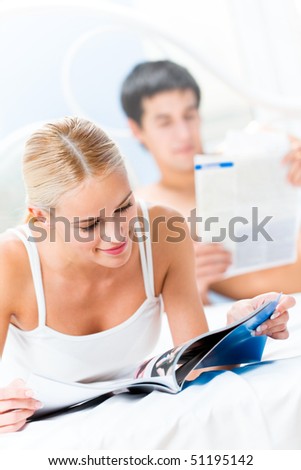 Young couple reading magazine and newspaper at bedroom