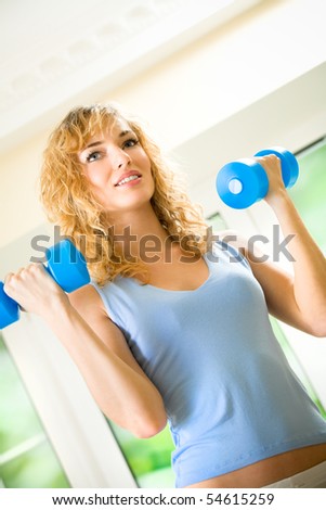 Young happy woman exercising with dumbbells at home