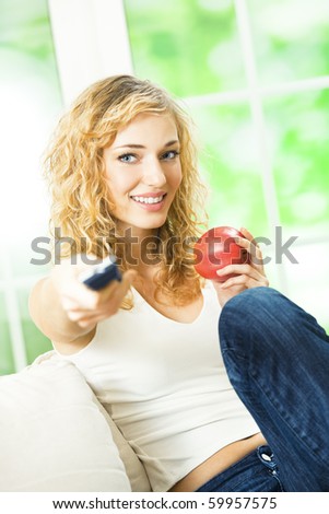 Young happy woman with apple, watching TV at home