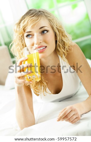 Happy young woman with juice of tropical fruit on bed