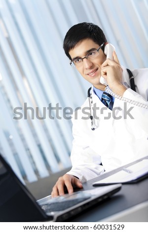 Successful doctor with phone and laptop, at office