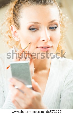 Young woman with mirror and makeup brush indoors