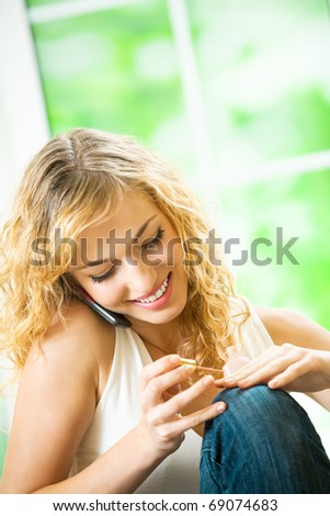 Portrait of young happy smiling woman making manicure and talking on cellphone at home