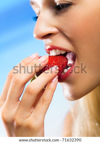 Young beautiful happy smiling woman eating strawberry on sea beach