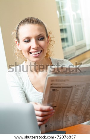 Young happy smiling woman with newspaper and laptop, at home