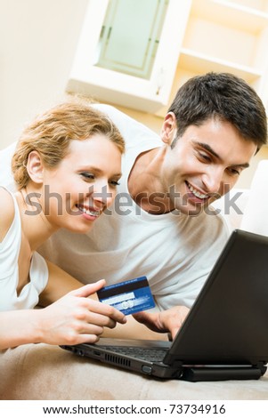 Young happy smiling couple with laptop, paying by credit card in internet store, at home