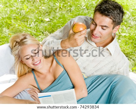 Young happy couple reading together newspaper outdoors
