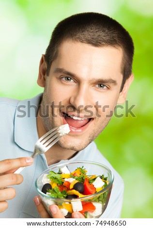 Young smiling man eating salad, outdoors