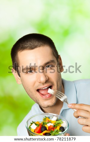 Portrait of young happy man eating salad, outdoors. You can use top part for slogan or text.