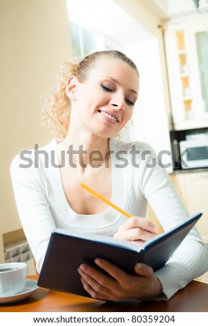 Young smiling woman with notebook or organiser at home