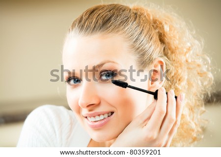 Young woman applying mascara with lash brush at home