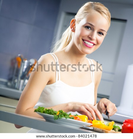 Young happy smiling woman making salad at kitchen