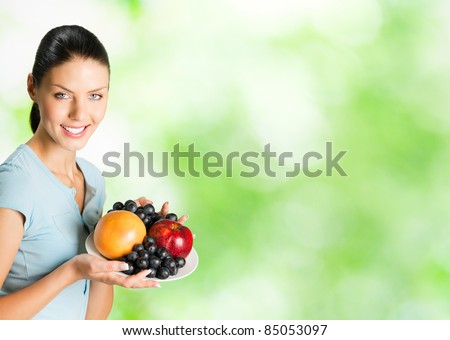 Young happy smiling woman with plate of fruits, outdoor. You can use right part for slogan, big text or banner.