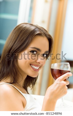 Portrait of happy smiling young attractive woman with glass of red wine, at home