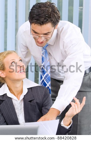 Two happy smiling cheerful businesspeople, or business person and client, working with laptop at office