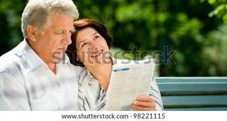 Happy smiling attractive senior couple reading together, outdoors, with copyspace