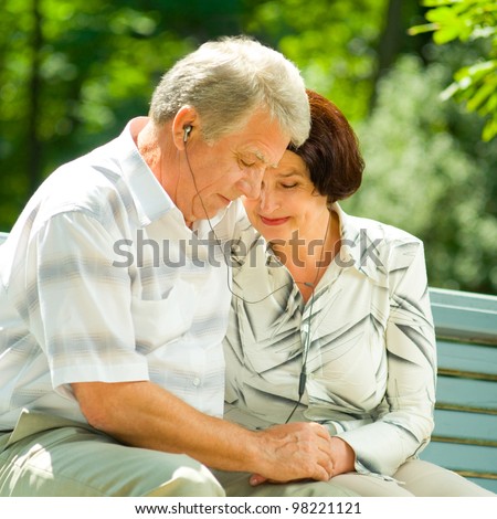 Happy smiling cheerful senior couple listening music or audio book in headset or praying together, outdoors