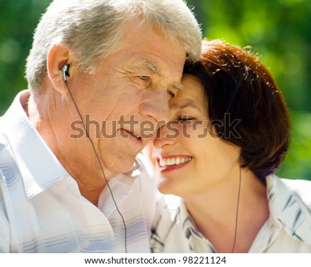 Happy smiling cheerful senior couple listening music or audio book in headset or praying together, outdoors