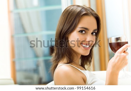 Portrait of happy smiling young attractive woman with glass of red wine, at home, with copyspace