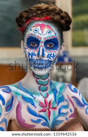 A gorgeous Hispanic Brunette model poses with traditional skull sugar makeup paint for a Mexican festival.