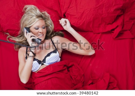 Blond model lying in bed while talking on the phone while being photographed from above.