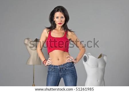A brunette model wearing a red shirt in the studio with mannequins in the background.