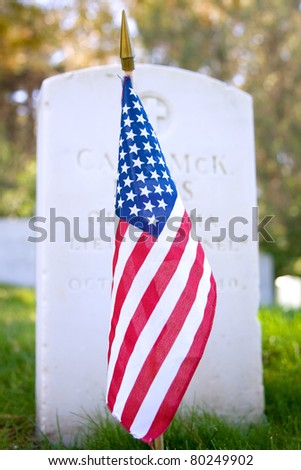 American flag in front of a gravestone in a military cemetery