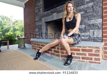 Blonde model posing in an against a fireplace in an outdoor environment