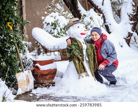 Woman is posing with a snowman in her front yard during snow storm