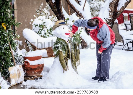 Woman is making a snowman in her front yard during snow storm