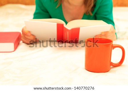 Home reading. Unrecognizable woman reading book with cup of coffee at home.