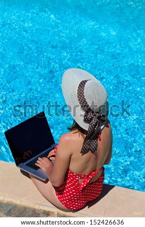 working on vacation concept. Young woman with laptop near the pool