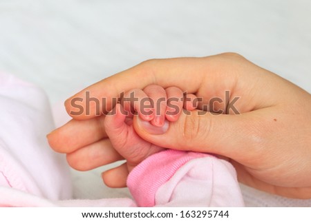 Newborn baby is held by the hand the parent. Care and support.