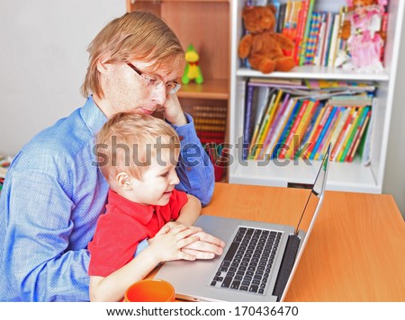 father in business style with little son working on laptop at home