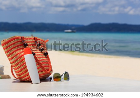 bag, sun glasses and suncream on tropical beach, vacation concept