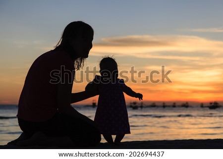 Silhouette of mother and little daughter on sunset beach