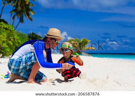 father and son playing with water guns on tropical beach
