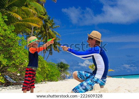 father and son playing with water guns on tropical beach