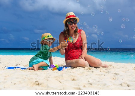 mother and son making soap bubbles on tropical beach