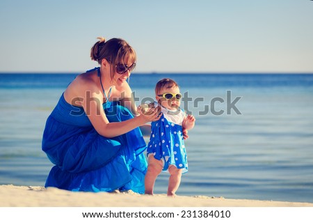 mother teaching her daughter to walk her first steps on tropical beach