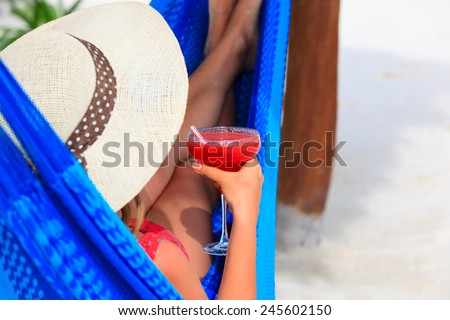 woman with cocktail relaxed in hammock on tropical beach