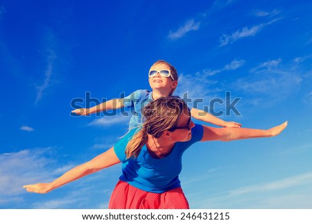 Mother and little son playing airplane on blue summer sky