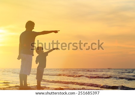 father and son at sunset beach, pointing at the sun