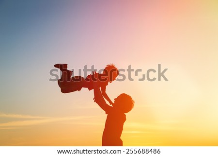 father and  little son silhouettes play at sunset