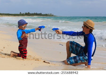father and son playing with water guns on summer beach