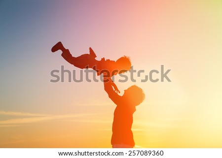 father and little son silhouettes play at sunset sky