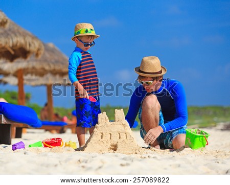 father and son building sand castle on tropical sand beach