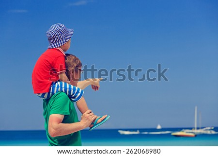 father and little son on shoulders pointing at the sea on summer beach