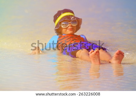 little boy playing with water on summer beach, focus on feet