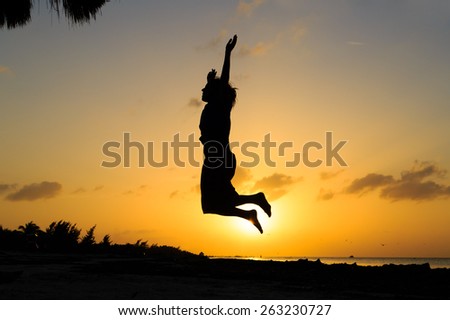 Silhouette of woman jumping on sunset beach